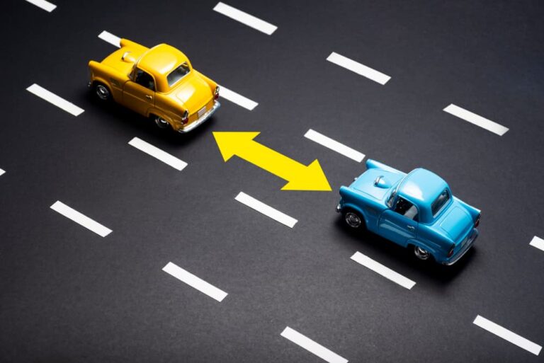 Two toy cars on the road one after another.