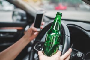 Drunk man driving a car on the road while holding a bottle of beer, representing the danger of drunk driving.