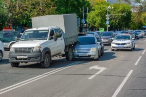 Two cars collide on a city street, surrounded by other vehicles. Road markings and a police car from the "Road Patrol Service" are visible.