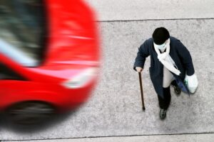 An elderly woman crossing a city street without taking precautions, with a car approaching.