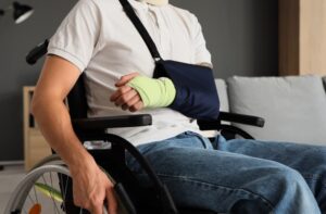 Injured young man with a broken arm sitting in a wheelchair at home after an accident, close-up