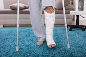 Man with a broken leg using crutches to walk on a blue carpet after a motorcycle accident