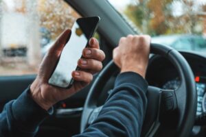 Car driver holding mobile smart phone over steering wheel