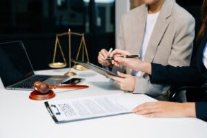 A lawyer and client discuss contract papers with a brass scale on the desk, symbolizing legal services, advice, and justice.