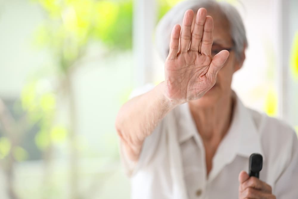 Elderly Asian woman raising her hand in a stop gesture, advocating against domestic violence and supporting women's rights.