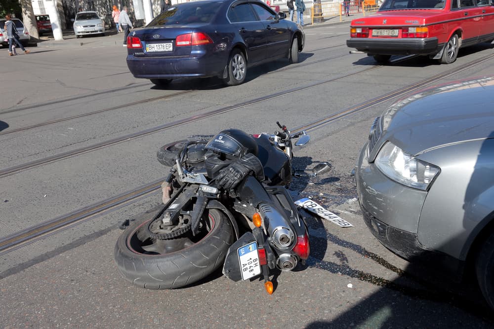 Accident between a car and motorcycle: bike crashed into the car after losing control on wet asphalt. First aid and insurance agent present.