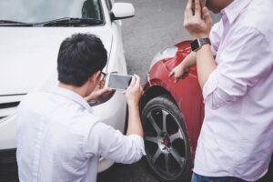 Two drivers arguing after a car accident, making phone calls to insurance agents and taking photos of the scene, illustrating traffic accident and insurance concept.