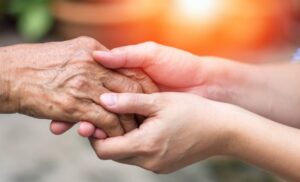 Caregiver holding an elderly person's hand in hospice care, symbolizing kindness and support.